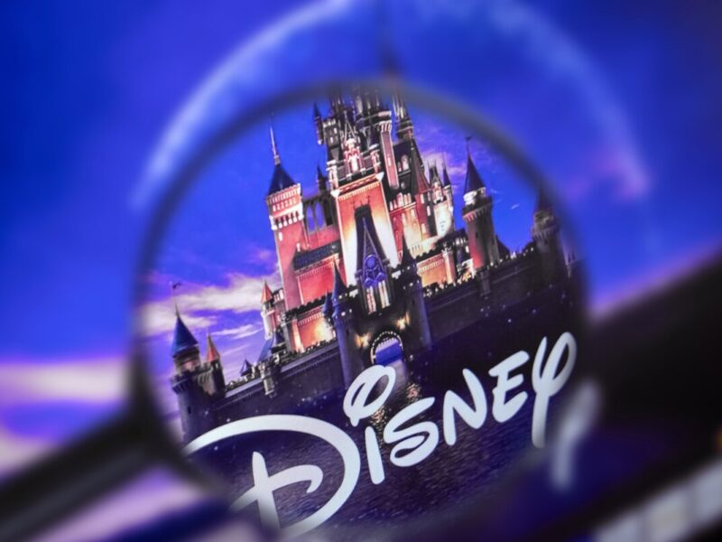 Une loupe se concentre sur le logo Disney avec un château en arrière-plan dans un ciel bleu et violet, soulignant la présence emblématique de Disney et ses obligations en 2020.