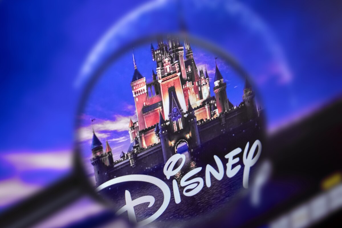 Une loupe se concentre sur le logo Disney avec un château en arrière-plan dans un ciel bleu et violet, soulignant la présence emblématique de Disney et ses obligations en 2020.