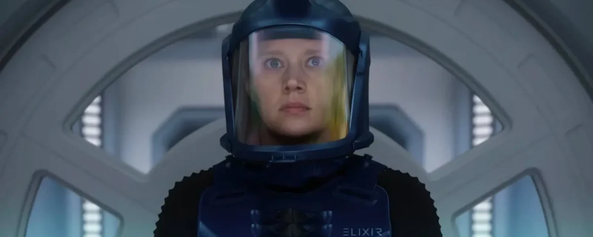 Une personne portant une combinaison de protection bleue et un casque se tient devant une porte circulaire à l'intérieur d'un décor futuriste, rappelant des scènes du film "In The Blink Of An Eye" d'Andrew Stanton, qui sera bientôt disponible sur Disney+.