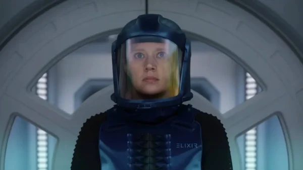 Une personne portant une combinaison de protection bleue et un casque se tient devant une porte circulaire à l'intérieur d'un décor futuriste, rappelant des scènes du film "In The Blink Of An Eye" d'Andrew Stanton, qui sera bientôt disponible sur Disney+.