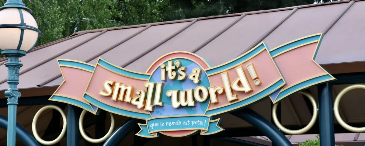 Panneau "it's a small world !" avec traduction en français, monté sur une structure de couleur pastel à Disneyland Paris, entourée d'arbres - l'un des charmants manèges adaptés enfants parfaits pour les familles.