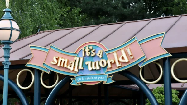 Panneau "it's a small world !" avec traduction en français, monté sur une structure de couleur pastel à Disneyland Paris, entourée d'arbres - l'un des charmants manèges adaptés enfants parfaits pour les familles.