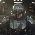 Un Mandalorien en armure métallique pilote un vaisseau spatial, avec Grogu, la petite créature verte, assis à proximité dans le cockpit.
