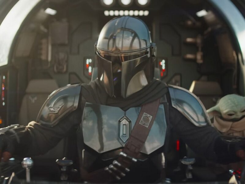 Un Mandalorien en armure métallique pilote un vaisseau spatial, avec Grogu, la petite créature verte, assis à proximité dans le cockpit.