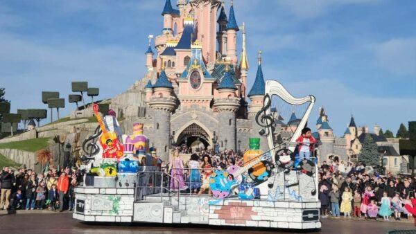 Un char de parade avec des personnages de Disney Pixar passe devant le château de la Belle au bois dormant à Disneyland Paris, sous le regard de la foule dans un ciel bleu clair.