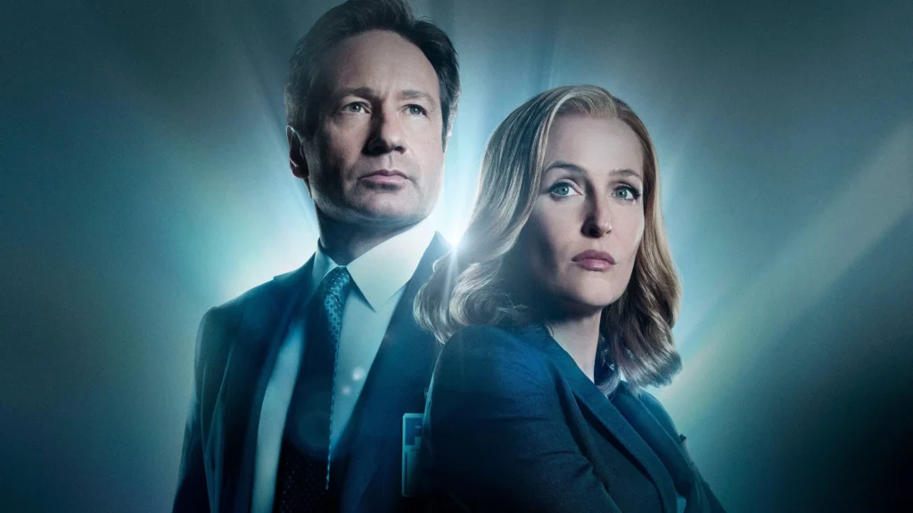 Deux personnes en tenue de travail se tiennent dos à dos avec des expressions sérieuses, éclairées par une lumière bleue provenant de l'arrière, évoquant l'atmosphère mystérieuse de The X-files et rappelant les rôles emblématiques de Gillian Anderson.