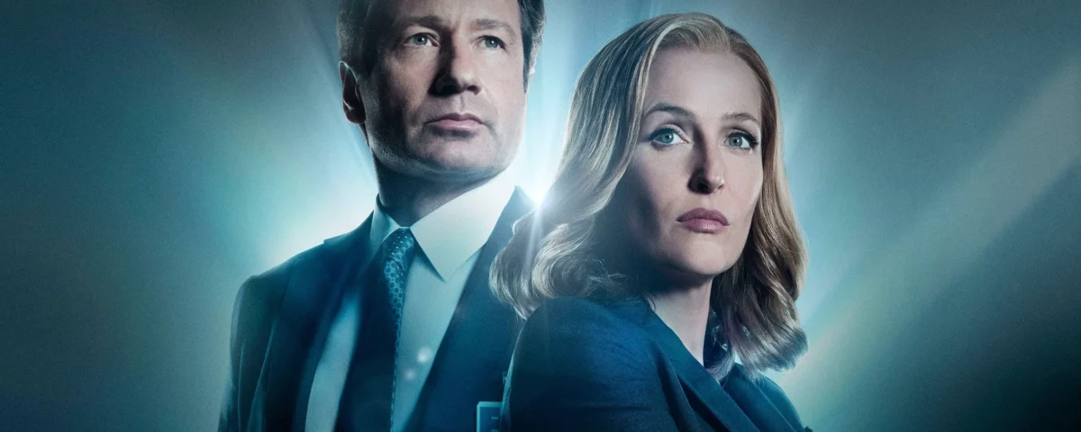 Deux personnes en tenue de travail se tiennent dos à dos avec des expressions sérieuses, éclairées par une lumière bleue provenant de l'arrière, évoquant l'atmosphère mystérieuse de The X-files et rappelant les rôles emblématiques de Gillian Anderson.