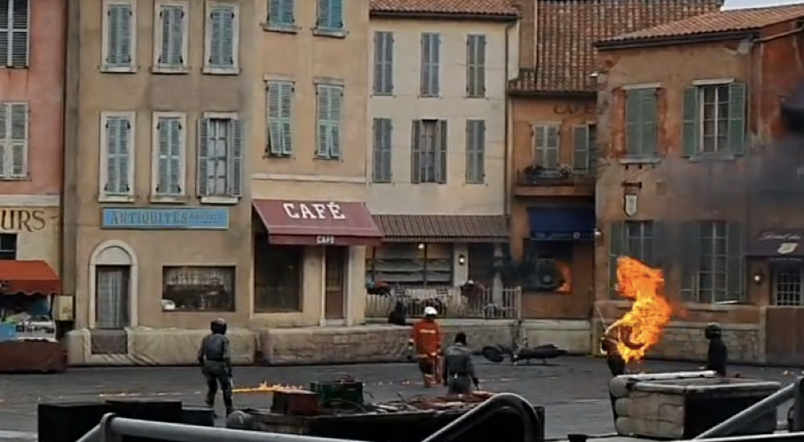 Une scène de Moteurs Action Stunt Show montre plusieurs personnes en tenue de protection sur un plateau de rue, avec une personne engloutie dans les flammes et des incendies contrôlés brûlant à proximité, avant sa fermeture le 13 mars 2020.