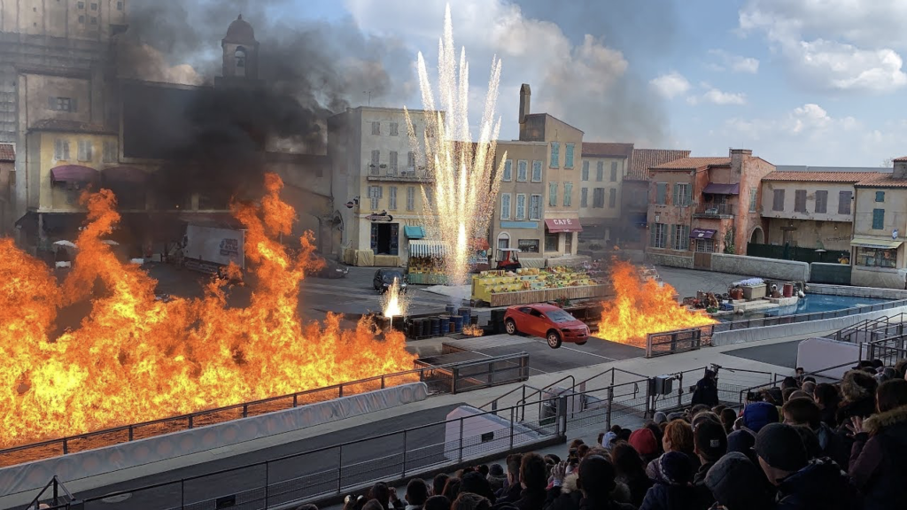 Une voiture rouge est garée sur une scène extérieure avec de grandes flammes et des feux d'artifice pendant le Moteurs Action Stunt Show Spectacular, sous le regard des spectateurs depuis les tribunes avant sa fermeture le 13 mars 2020.