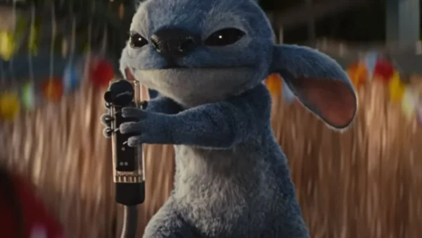 Une créature bleue animée avec de grandes oreilles, inspirée de Lilo & Stitch, tient un microphone tout en se tenant à l'extérieur.