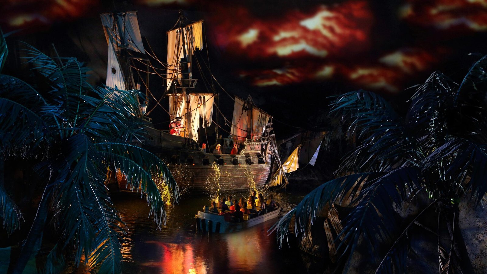 Un bateau de pirates aux voiles en lambeaux fait face à un petit bateau de personnes sur un cours d'eau sombre, entouré de palmiers artificiels sous un ciel rouge dramatique - l'une des attractions à sensations de Disneyland Paris.