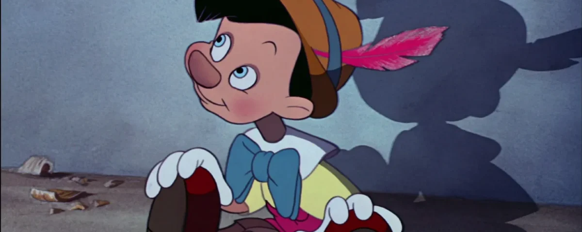 La marionnette animée en bois, coiffée d'un chapeau à plumes, est assise sur le sol et regarde vers le haut, projetant une ombre de forme humaine - un clin d'œil à l'influence culturelle que l'on retrouve dans les films classiques de Disney.