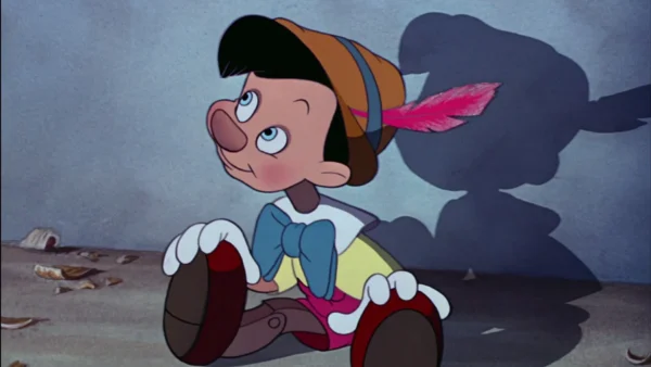 La marionnette animée en bois, coiffée d'un chapeau à plumes, est assise sur le sol et regarde vers le haut, projetant une ombre de forme humaine - un clin d'œil à l'influence culturelle que l'on retrouve dans les films classiques de Disney.
