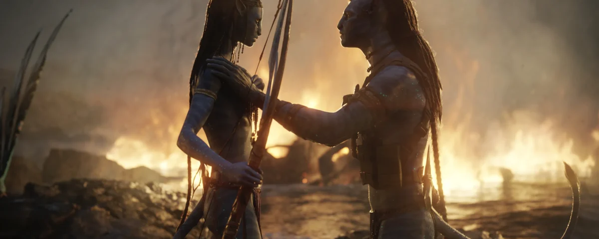 Deux personnages humanoïdes à la peau bleue d'Avatar Fire And Ash se font face avec des armes, du feu et de la fumée tourbillonnant en arrière-plan sur un paysage rocheux - une scène saisissante d'un film Disney qui a fait sensation au box-office mondial.