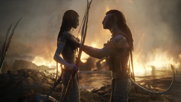 Deux personnages humanoïdes à la peau bleue d'Avatar Fire And Ash se font face avec des armes, du feu et de la fumée tourbillonnant en arrière-plan sur un paysage rocheux - une scène saisissante d'un film Disney qui a fait sensation au box-office mondial.