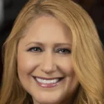 Une femme aux longs cheveux blonds sourit à l'appareil photo dans un portrait en gros plan, reflétant la chaleur et le charme que l'on retrouve souvent dans les émissions de Disney Entertainment Television.