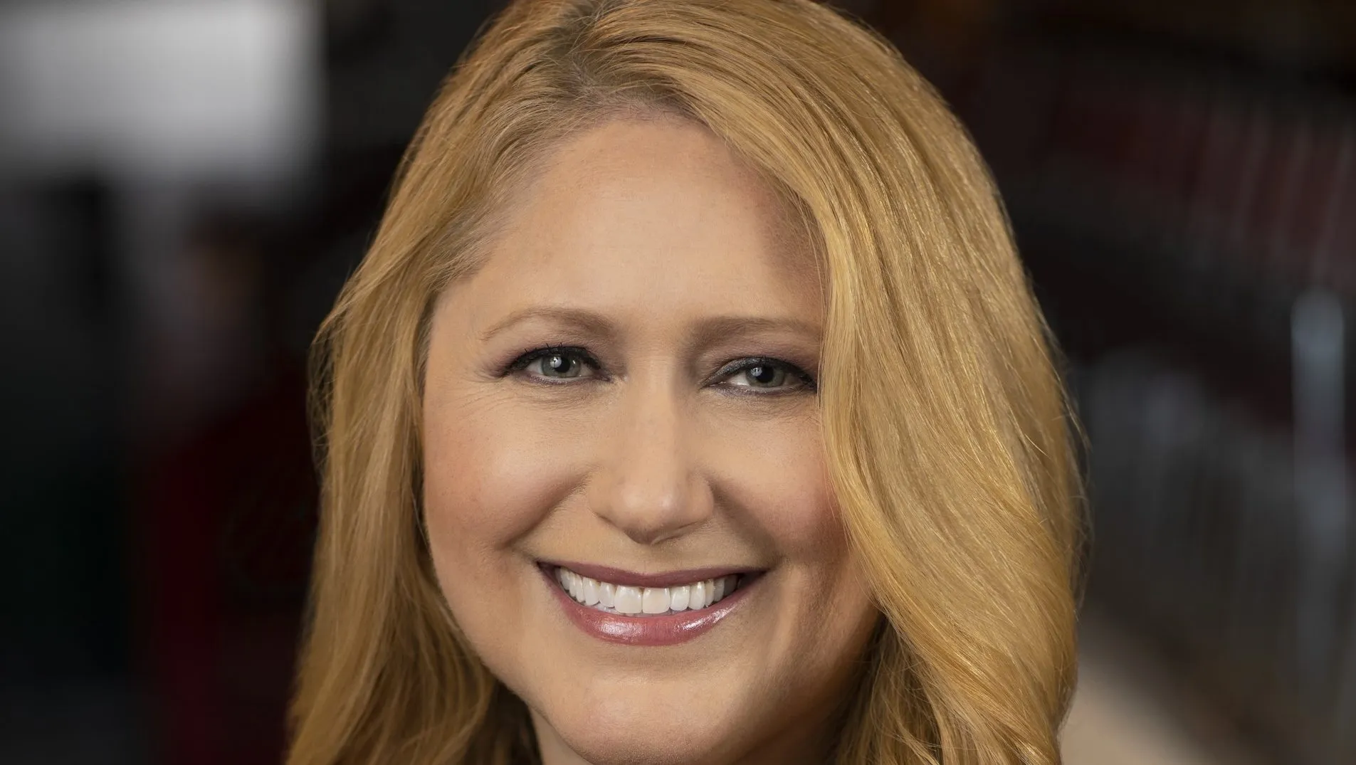 Une femme aux longs cheveux blonds sourit à l'appareil photo dans un portrait en gros plan, reflétant la chaleur et le charme que l'on retrouve souvent dans les émissions de Disney Entertainment Television.