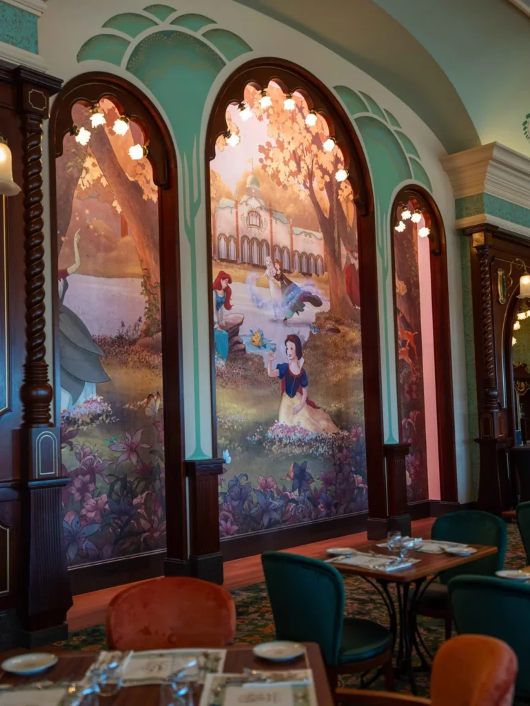 Une grande fresque représentant Blanche-Neige et des animaux de la forêt décore le mur voûté du Regal View Restaurant à Disneyland Paris, où des tables dressées et des chaises colorées créent une atmosphère magique.