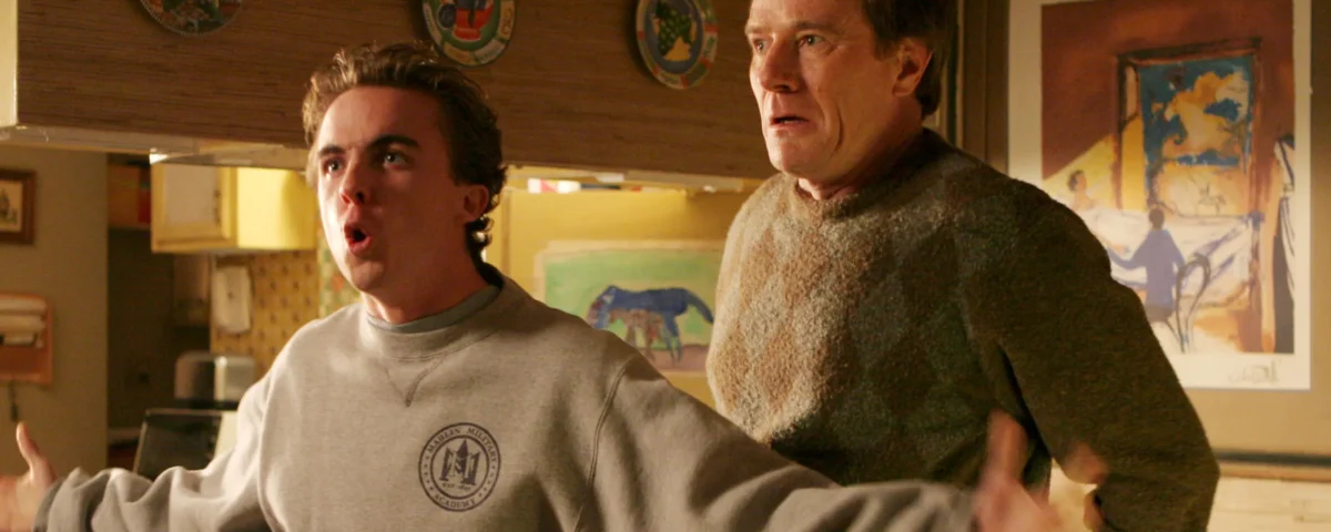 Deux hommes se tiennent dans une cuisine ; le plus jeune, qui ressemble à Malcolm (Frankie Muniz), parle avec emphase, les bras tendus, tandis que le plus âgé, qui ressemble beaucoup au personnage de Bryan Cranston, regarde la scène d'un air inquiet.