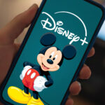 Une main tenant un smartphone affiche le logo Disney+ avec une image de Mickey Mouse sur l'écran, mettant en avant des vidéos verticales conçues pour renforcer l'engagement des abonnés.