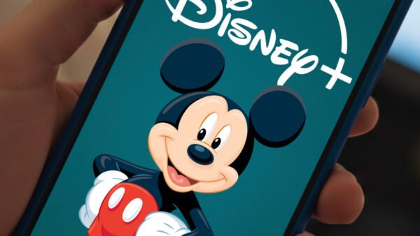 Une main tenant un smartphone affiche le logo Disney+ avec une image de Mickey Mouse sur l'écran, mettant en avant des vidéos verticales conçues pour renforcer l'engagement des abonnés.