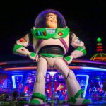 Une grande statue de Buzz l'Éclair se dresse devant le bâtiment futuriste de Space Mountain, illuminé de nuit, dans le parc d'attractions de Disney World.