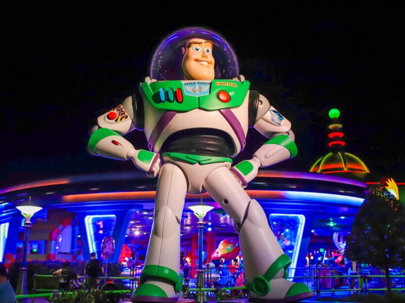 Une grande statue de Buzz l'Éclair se dresse devant le bâtiment futuriste de Space Mountain, illuminé de nuit, dans le parc d'attractions de Disney World.