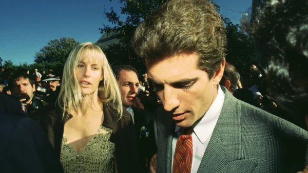 Une femme et un homme en tenue de soirée marchent à l'extérieur dans une foule, avec des arbres et un ciel dégagé en arrière-plan, évoquant l'élégance d'une scène de Love Story Disney+.