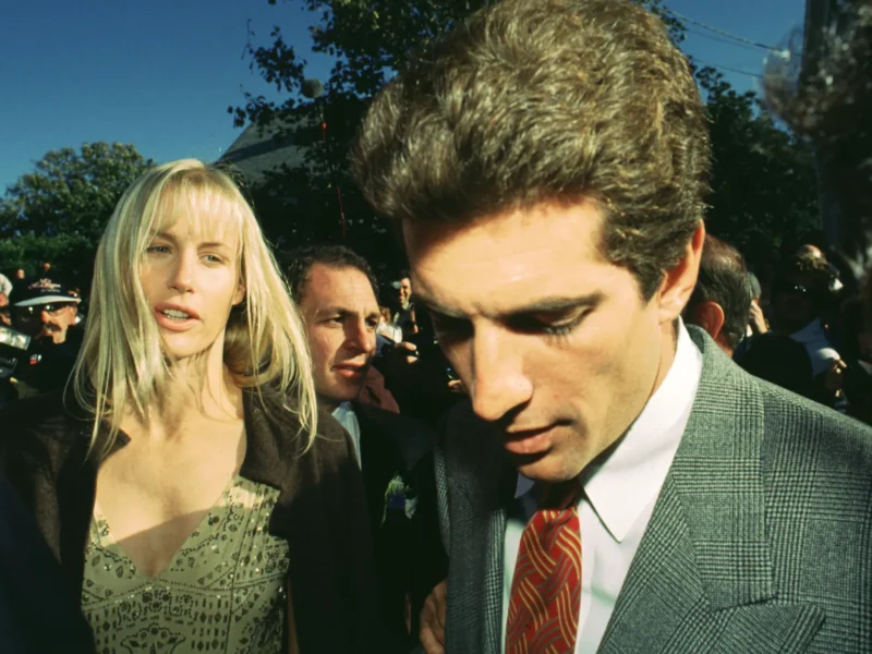 Une femme et un homme en tenue de soirée marchent à l'extérieur dans une foule, avec des arbres et un ciel dégagé en arrière-plan, évoquant l'élégance d'une scène de Love Story Disney+.