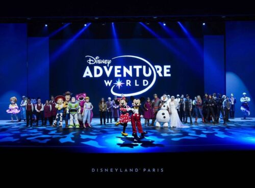 Un groupe de personnages et de personnes de Disney se tient sur scène devant un grand panneau "Disney Adventure World", célébrant la nouvelle campagne à Disneyland Paris.