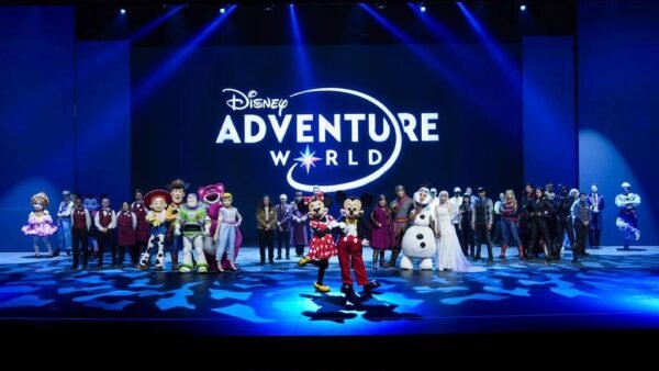 Un groupe de personnages et de personnes de Disney se tient sur scène devant un grand panneau "Disney Adventure World", célébrant la nouvelle campagne à Disneyland Paris.