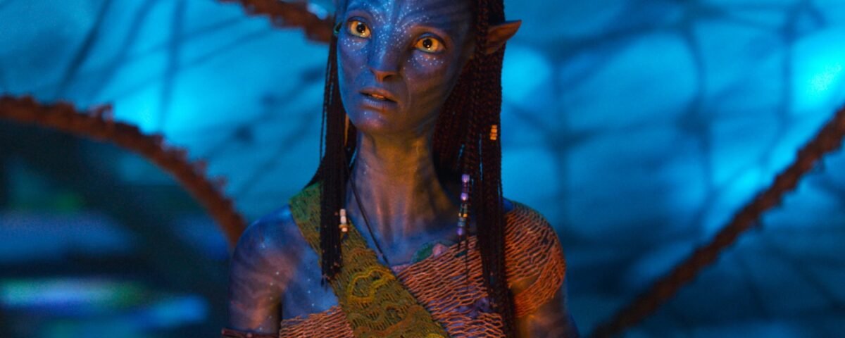 Un extraterrestre humanoïde à la peau bleue d'Avatar, aux cheveux tressés et aux accessoires perlés, se tient sur un fond bleu lumineux, vêtu d'une guêpe à motifs - un look emblématique du film oscarisé pour Meilleurs Effets Visuels.