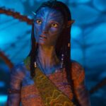 Un extraterrestre humanoïde à la peau bleue d'Avatar, aux cheveux tressés et aux accessoires perlés, se tient sur un fond bleu lumineux, vêtu d'une guêpe à motifs - un look emblématique du film oscarisé pour Meilleurs Effets Visuels.