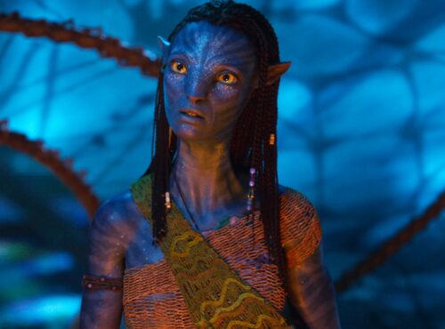 Un extraterrestre humanoïde à la peau bleue d'Avatar, aux cheveux tressés et aux accessoires perlés, se tient sur un fond bleu lumineux, vêtu d'une guêpe à motifs - un look emblématique du film oscarisé pour Meilleurs Effets Visuels.