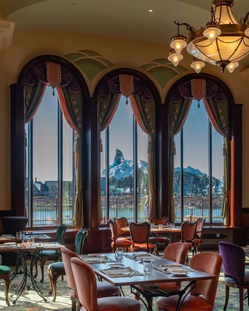 L'intérieur du restaurant Regal View est élégant, avec des tables dressées et de grandes fenêtres cintrées offrant une vue imprenable sur Disneyland Paris et ses parcs d'attractions à l'extérieur.