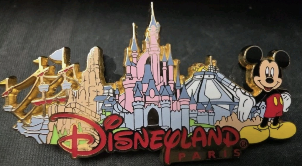 Aimant souvenir de Disneyland Paris représentant le château de la Belle au bois dormant, les attractions emblématiques du parc, le logo de Disneyland Paris, un Mickey Mouse debout à droite, et un clin d'œil à l'échange d'épingles depuis le 6 octobre 2001.