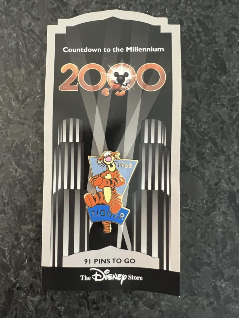 Un pin's Disney Store à l'effigie de Tigrou est présenté sur une carte "Countdown to the Millennium 2000", célébrant le Pin Trading avec "91 pins to go" écrit au bas de la carte.