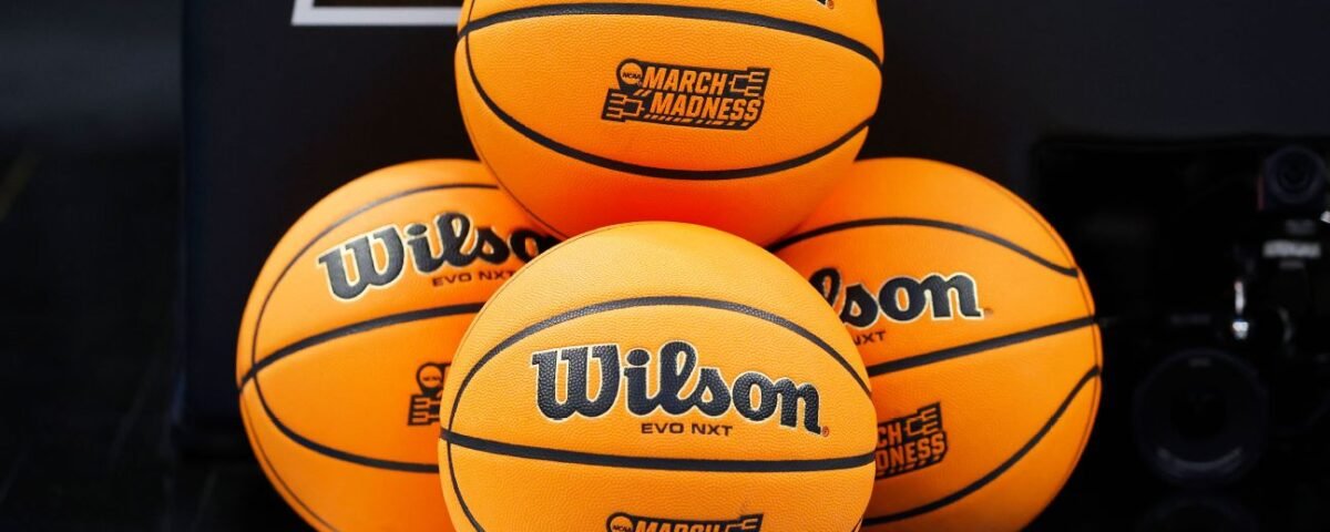 Quatre ballons de basket Wilson EVO NXT avec les logos "March Madness" sont empilés sur un terrain de basket, capturant l'excitation de NCAA 2026 et l'esprit du basket américain pendant la saison des tournois.
