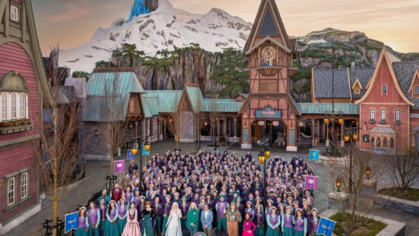 Un grand groupe de personnes en costumes thématiques pose devant une place de village inspirée d'Arendelle, avec des bâtiments alpins et une montagne enneigée en arrière-plan, dans le Monde de Frozen de Disneyland Paris.