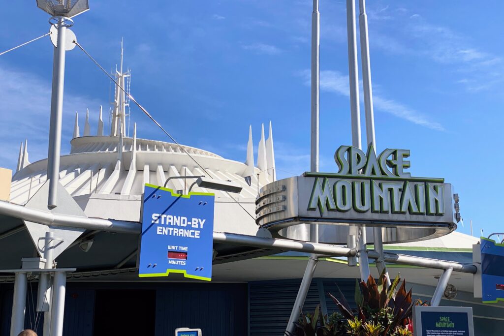 Entrée de Space Mountain à Disney World, avec le bâtiment futuriste de l'attraction et le panneau des temps d'attente sous un ciel bleu clair.