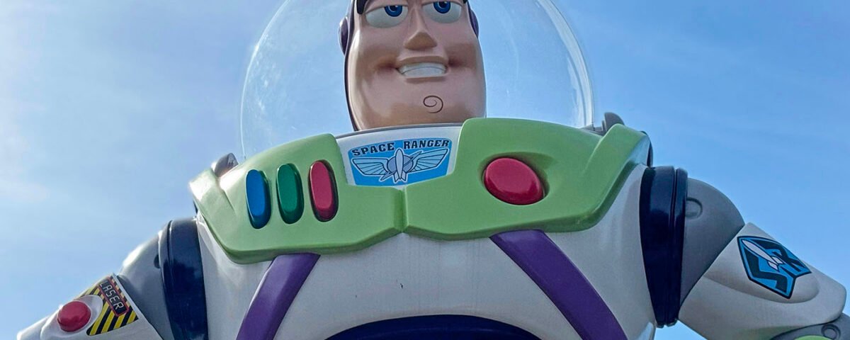 Gros plan d'une figurine de Buzz l'éclair dans sa combinaison spatiale blanche, verte et violette, sur fond de ciel bleu clair, rappelant l'attraction Buzz l'éclair laser de Disneyland Paris.