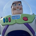Gros plan d'une figurine de Buzz l'éclair dans sa combinaison spatiale blanche, verte et violette, sur fond de ciel bleu clair, rappelant l'attraction Buzz l'éclair laser de Disneyland Paris.