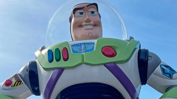 Gros plan d'une figurine de Buzz l'éclair dans sa combinaison spatiale blanche, verte et violette, sur fond de ciel bleu clair, rappelant l'attraction Buzz l'éclair laser de Disneyland Paris.