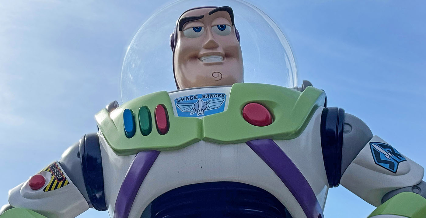 Gros plan d'une figurine de Buzz l'éclair dans sa combinaison spatiale blanche, verte et violette, sur fond de ciel bleu clair, rappelant l'attraction Buzz l'éclair laser de Disneyland Paris.