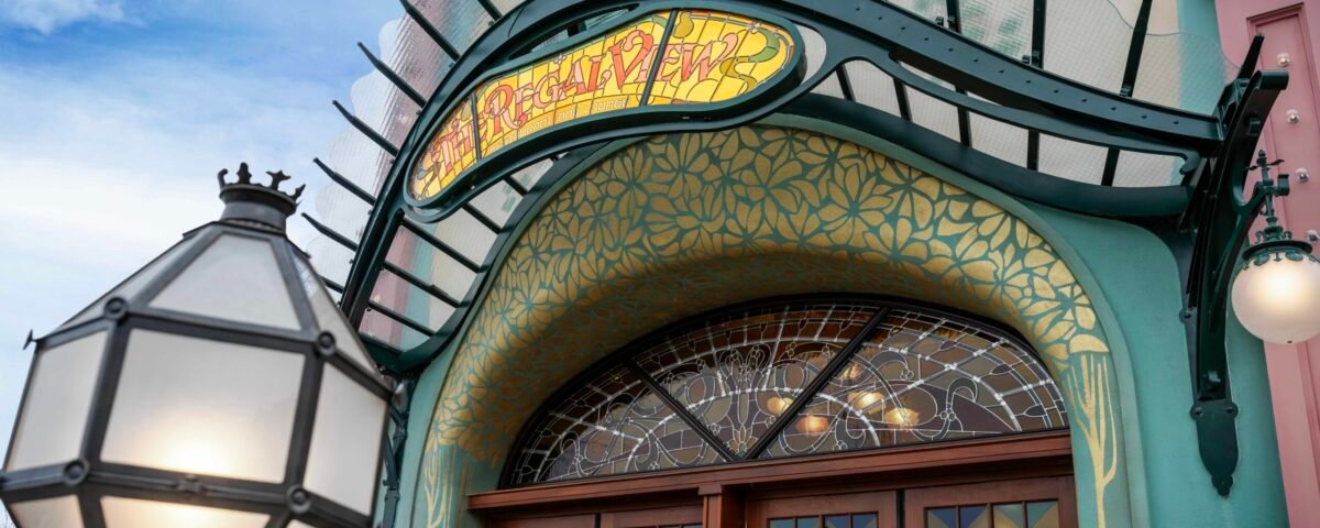 Entrée de style Art nouveau du restaurant Regal View, avec une enseigne en vitrail au-dessus de doubles portes en bois, des ornements réalisés par les Ateliers Schaffner et un lampadaire décoratif, évoquant le charme de Disney Adventure World.