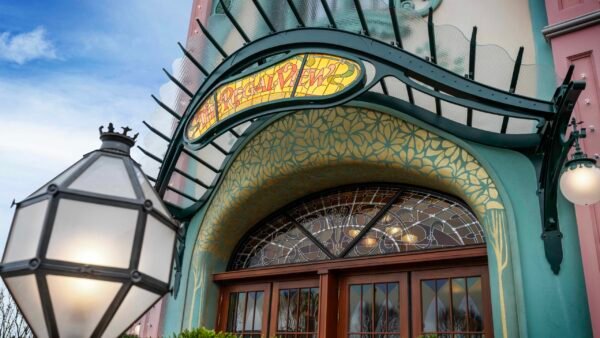 Entrée de style Art nouveau du restaurant Regal View, avec une enseigne en vitrail au-dessus de doubles portes en bois, des ornements réalisés par les Ateliers Schaffner et un lampadaire décoratif, évoquant le charme de Disney Adventure World.