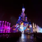 Le château de la Belle au bois dormant de Disneyland Paris s'illumine la nuit avec des lumières colorées, des fontaines d'eau et une image projetée d'Alice dans "Alice au pays des merveilles", créant une présence magique qui captive la perception des habitants et des visiteurs.