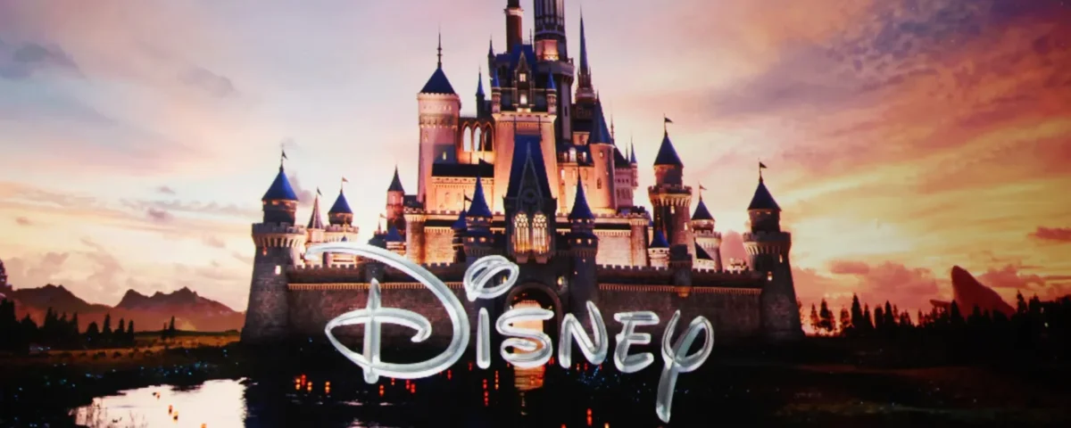 Un château aux flèches bleues se reflète dans un lac au coucher du soleil, tandis que le mot "Disney" apparaît en gros caractères sur l'image, soulignant subtilement la récente restructuration de l'entreprise.
