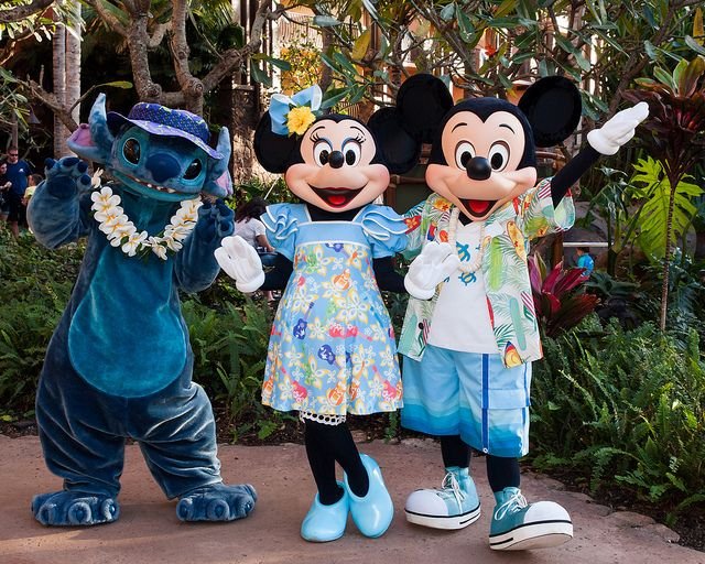 Stitch, Minnie Mouse et Mickey Mouse posent ensemble en plein air dans des tenues tropicales à Disneyland Paris pendant les Stitch Days, entourés de verdure luxuriante.
