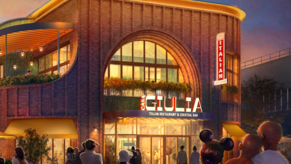 Au crépuscule, dans le Disney Village, près de Disneyland Paris, des gens se dirigent vers Casa Giulia, un restaurant italien moderne de deux étages, avec un éclairage chaleureux et une enseigne au néon au-dessus de l'entrée.